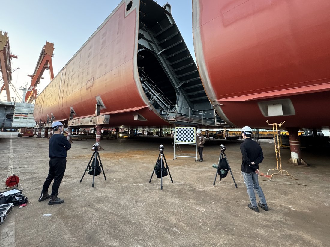 Stereo camera measurement setup between ship blocks at a shipyard — three tripod-mounted cameras and a checkerboard target